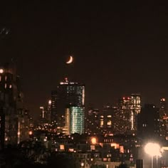 the city skyline is lit up at night with bright lights and moon in the sky