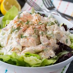 a white bowl filled with chicken salad next to a fork and lemon wedges on a table