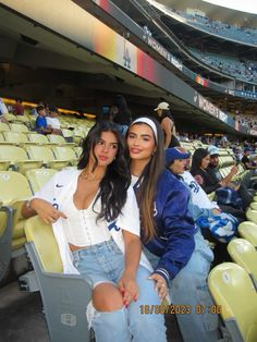 two young women sitting in the stands at a baseball game, posing for a photo