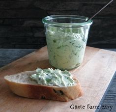 a piece of bread sitting on top of a wooden cutting board next to a jar of dip