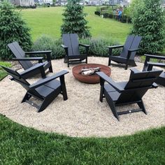 a fire pit surrounded by lawn chairs in the middle of a yard with grass and bushes