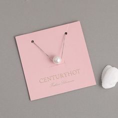 a pink card with a pearl on it next to a seashell and a pair of earrings