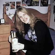 a woman sitting on a bed holding a bottle in her hand and smiling at the camera