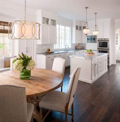 a kitchen and dining room with white cabinets, wood floors and an island in the middle