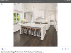 a large kitchen with white cabinets and wooden flooring, along with bar stools