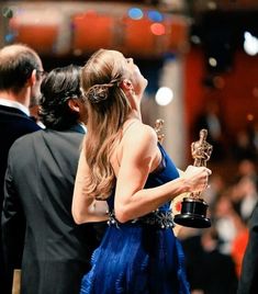 a woman in a blue dress holding an award and looking up at the sky with her eyes closed