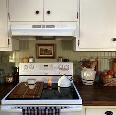 a stove top oven sitting inside of a kitchen next to white cupboards and drawers