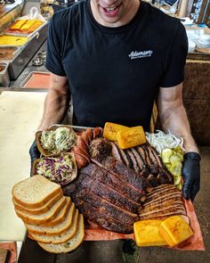 a man holding a platter of steak, bread and other foods in front of him