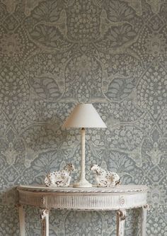 a white table with a lamp on it in front of a wallpapered background