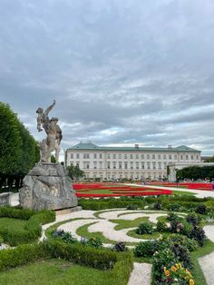 a statue in the middle of a garden with flowers around it and a building in the background