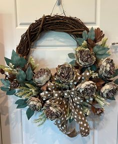 a wreath with flowers and leaves hanging on the front door to decorate it for christmas