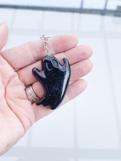 a hand holding a black cat shaped keychain on it's thumb,