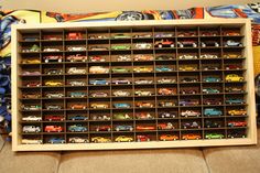 a wooden shelf filled with toy cars on top of a floor next to a pillow