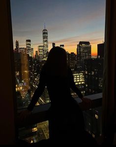 a woman standing in front of a window looking out at the city lights and skyscrapers