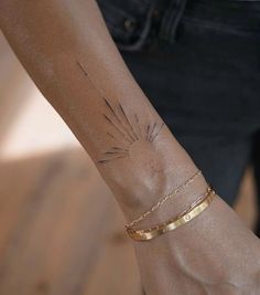 a woman's arm with a gold bracelet and sun tattoo on the left wrist