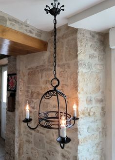 a chandelier with three candles hanging from it's sides in front of a stone wall