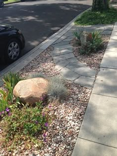 a black car parked on the side of a road next to a rock and plants