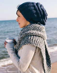 a woman is standing on the beach with a cup in her hand and looking at the water