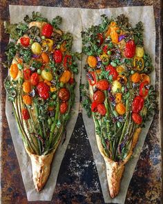 two pieces of pizza with vegetables on them sitting on top of parchment paper next to each other