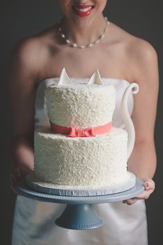 a woman is holding a cake with white frosting and pink ribbon on the top