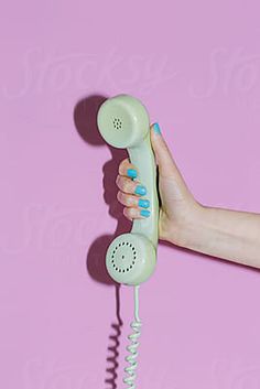 a woman's hand holding an old fashioned phone in front of a pink background