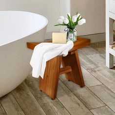 a white bath tub sitting next to a wooden table with flowers on top of it