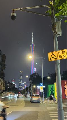 a city street at night with tall buildings in the background and cars driving down the road