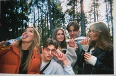 a group of people standing next to each other in front of trees with their mouths open