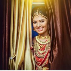 a woman in a red and gold bridal outfit is peeking out from behind a curtain