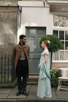 a man and woman dressed in period clothing standing on the sidewalk next to each other