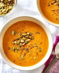 two bowls of carrot soup with pumpkin seeds and pistachios on the side