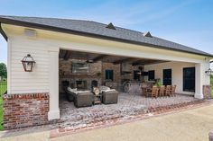 an outdoor living area with chairs and tables in front of a white house that has brick walls