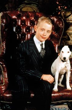 a young man in a suit sitting on a chair with his white dog next to him