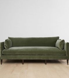 a green couch sitting on top of a hard wood floor next to a white wall