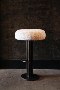 a white stool with a black base on concrete floor next to dark wall and cement floor