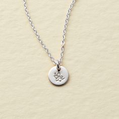 a silver necklace with a small flower on the front and a tiny round charm on the back