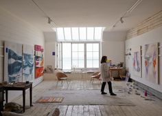 a woman is standing in an art studio with paintings on the walls and flooring