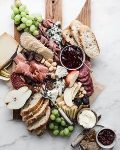 an assortment of cheeses, meats and bread on a cutting board with grapes