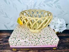 a wicker bowl sitting on top of a book next to flowers and a lemon