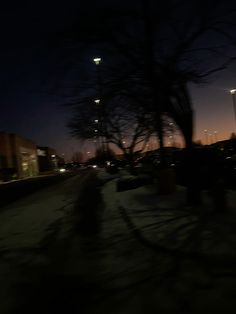 a blurry photo of a street at night with buildings in the back ground and lights on