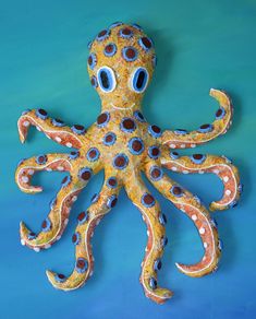 an orange and blue octopus sculpture sitting on top of a blue surface with eyes painted on it's head