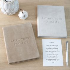 a table topped with two notebooks next to a white vase and a notepad