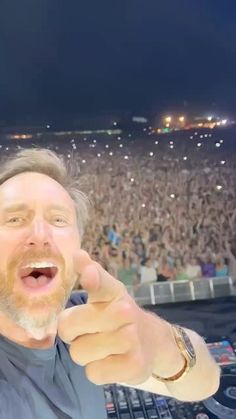 a man pointing at the camera in front of a large crowd with his fingers up