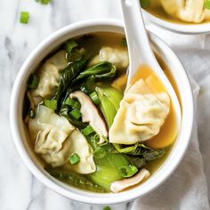 two white bowls filled with dumplings and vegetables on top of a marble countertop