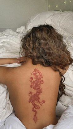 a woman laying in bed with a tattoo on her back