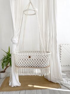 a white hammock hanging from the ceiling next to a potted plant on a rug