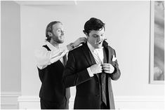 two men standing next to each other in front of a mirror and adjusting their ties