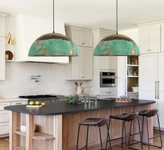 a kitchen with two pendant lights over the island and stools in front of it