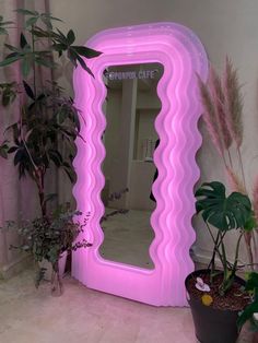 a pink mirror sitting on top of a floor next to potted plants and trees