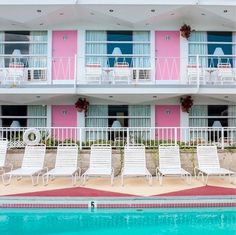 several lawn chairs sitting in front of a swimming pool next to a pink and white building